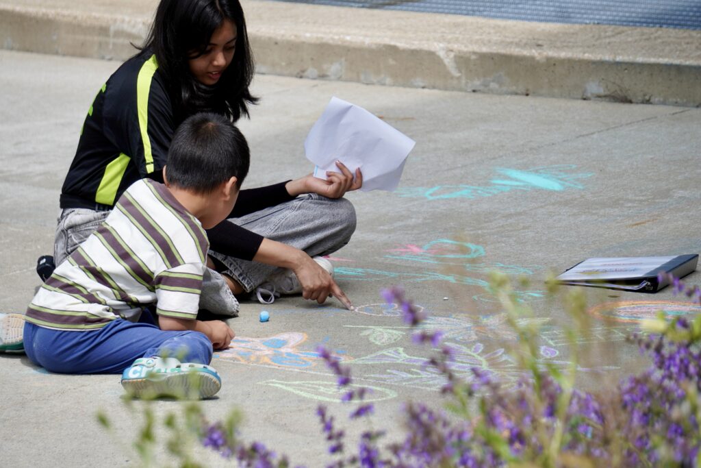 Kid with counselor drawing on the sidewalk with chalk